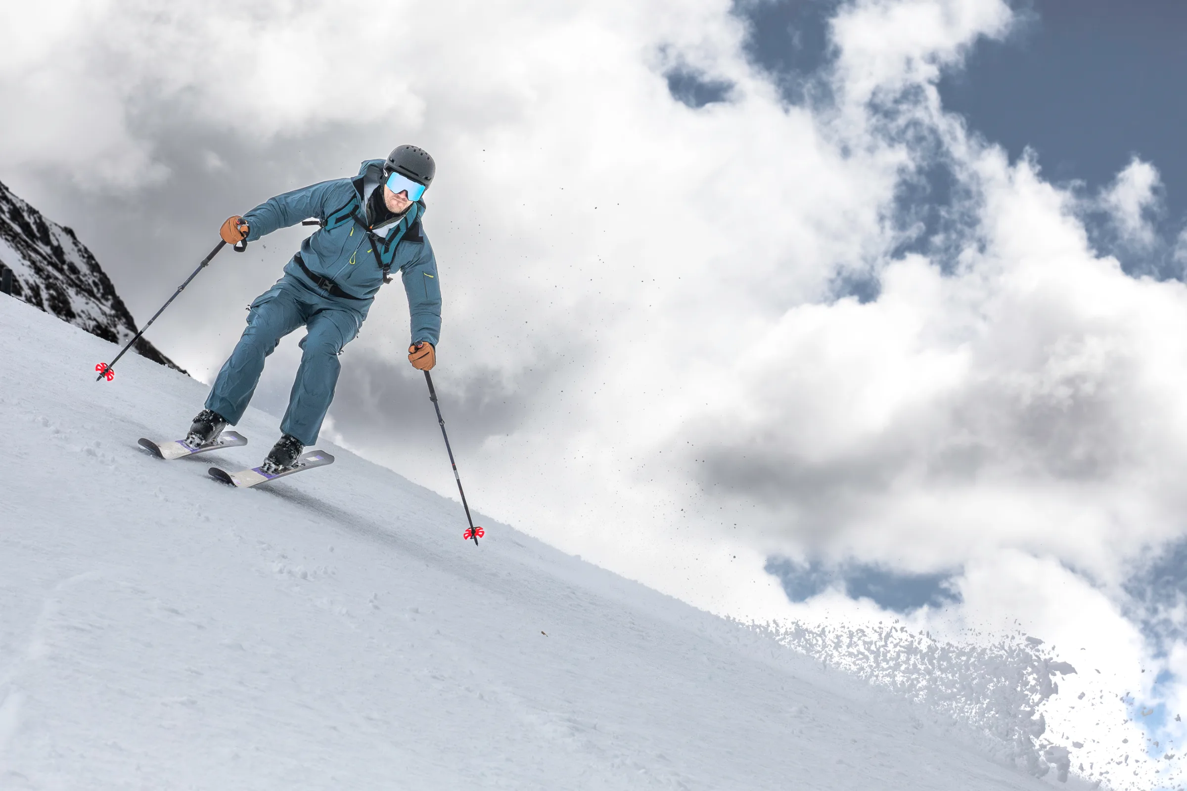 Simon Stickl fährt in blauer Skikleidung mit Helm und Rucksack einen Schneehang in Lenzerheide hinab, vor einem Himmel mit großen Wolken.