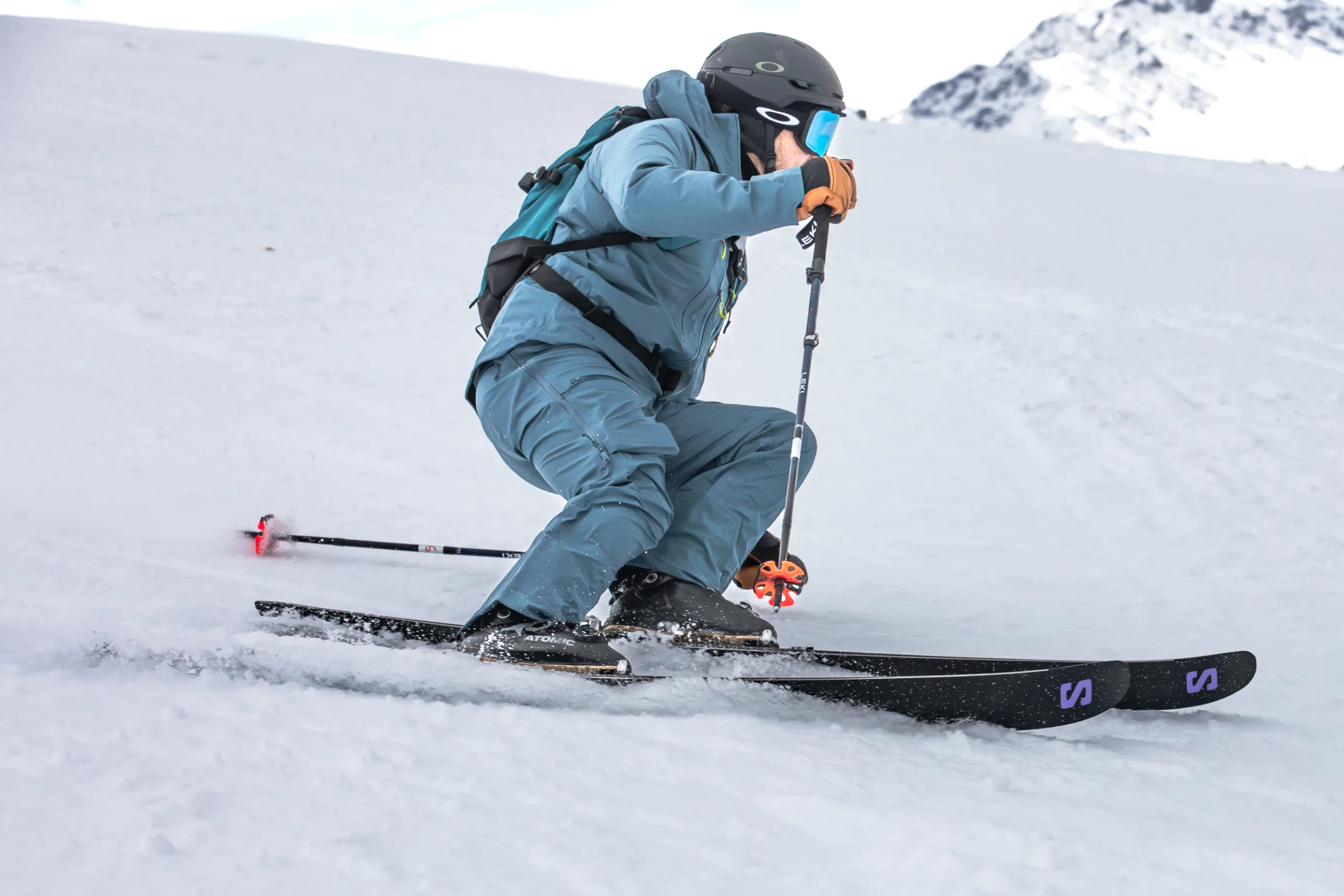 Simon Stickl fährt mit tief gebeugten Knien eine Kurve auf einem Schneehang, die Skistöcke in den Händen und verschneite Felsen im Hintergrund.
