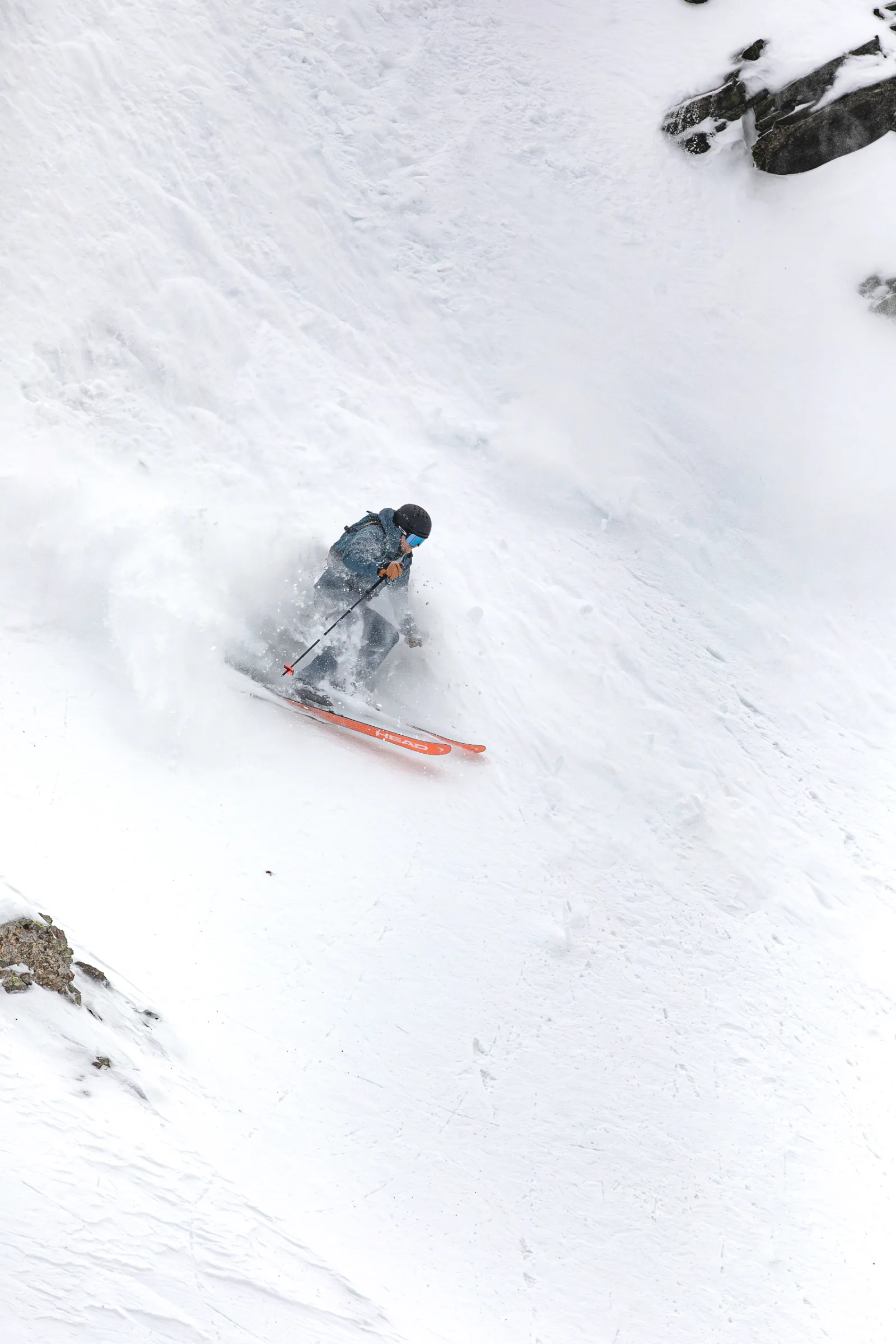 Simon Stickl fährt auf orangefarbenen Ski durch eine steile, felsgesäumte Schneerinne in Lenzerheide und wirbelt dabei Schnee auf.