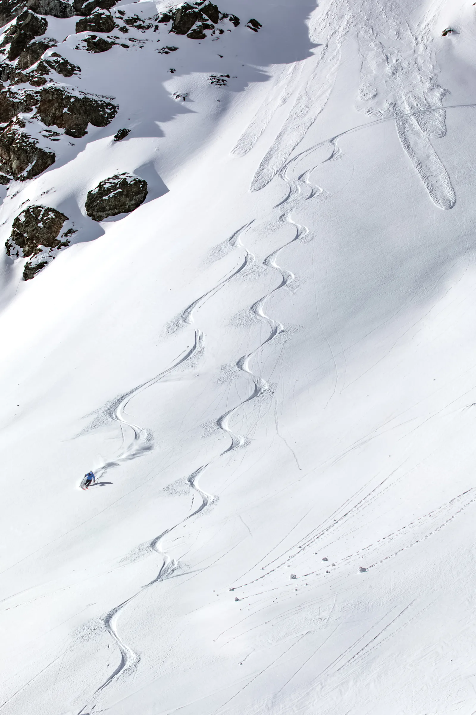 Simon Stickl zieht einen Schwung auf einem weiten Schneehang in Lenzerheide, über dem sich lange geschwungene Skispuren und dunkle Felsen erstrecken.