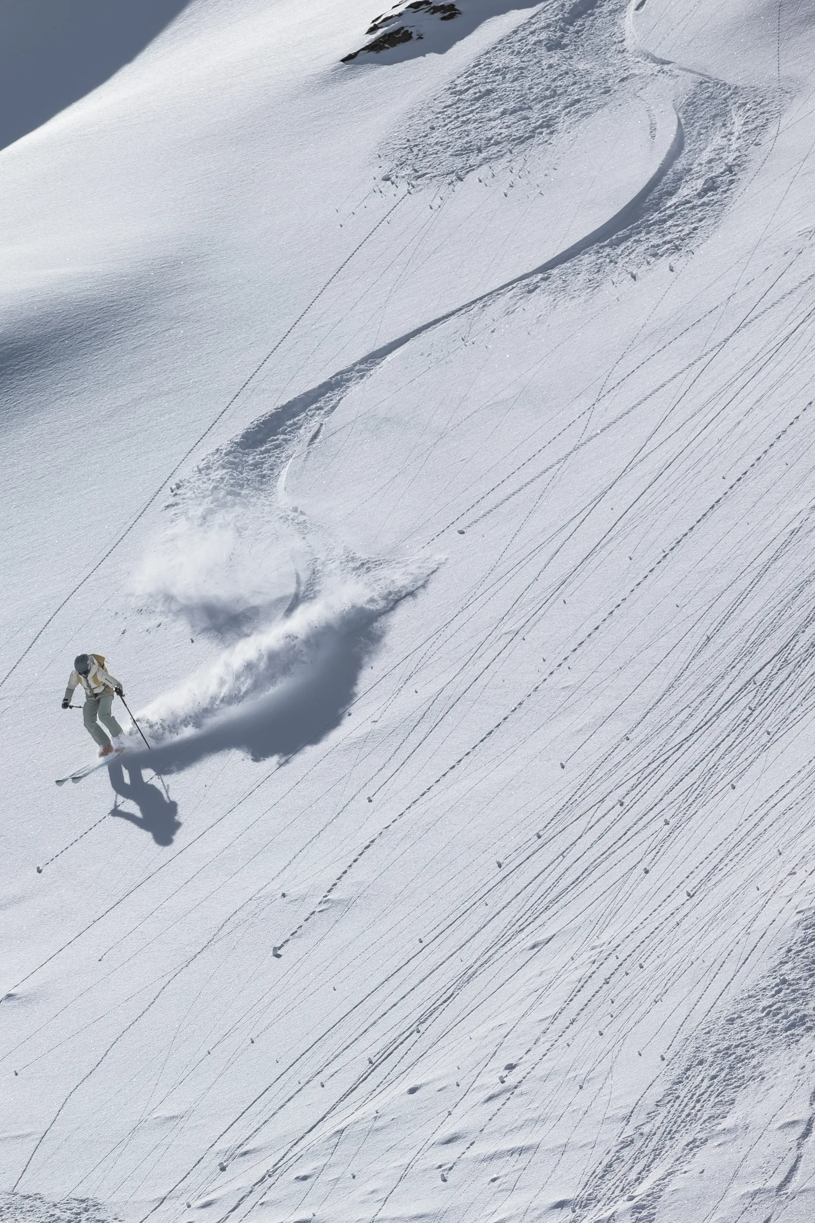 Sofia Muigg fährt nach links durch den Pulverschnee, während sich hinter ihr eine geschwungene Spur und eine breite Schneefahne über den Hang ziehen.