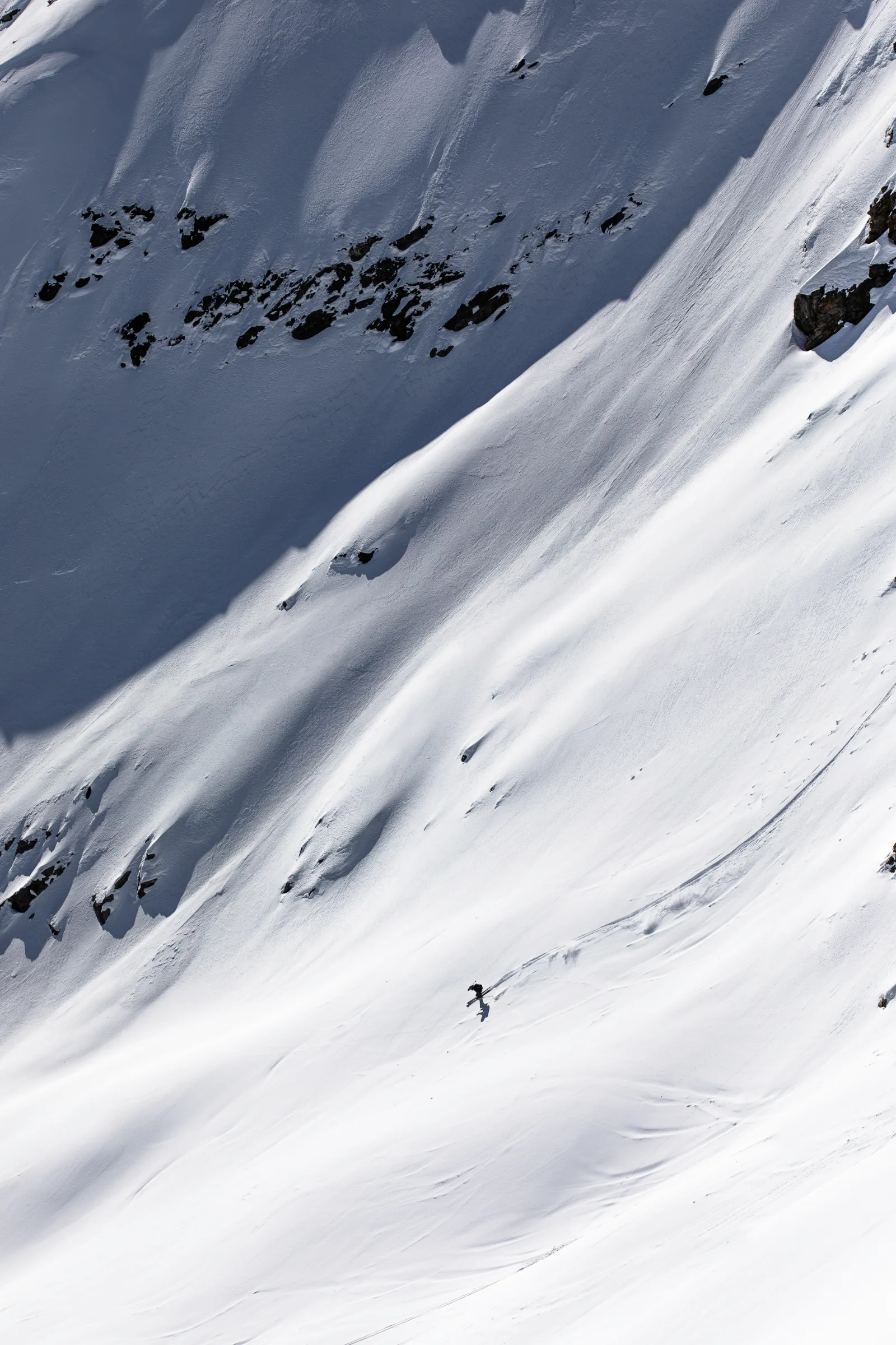 Valentin Rapp fährt über einen offenen Schneehang mit Licht- und Schattenflächen; seine lange geschwungene Spur zieht sich nach rechts oben.