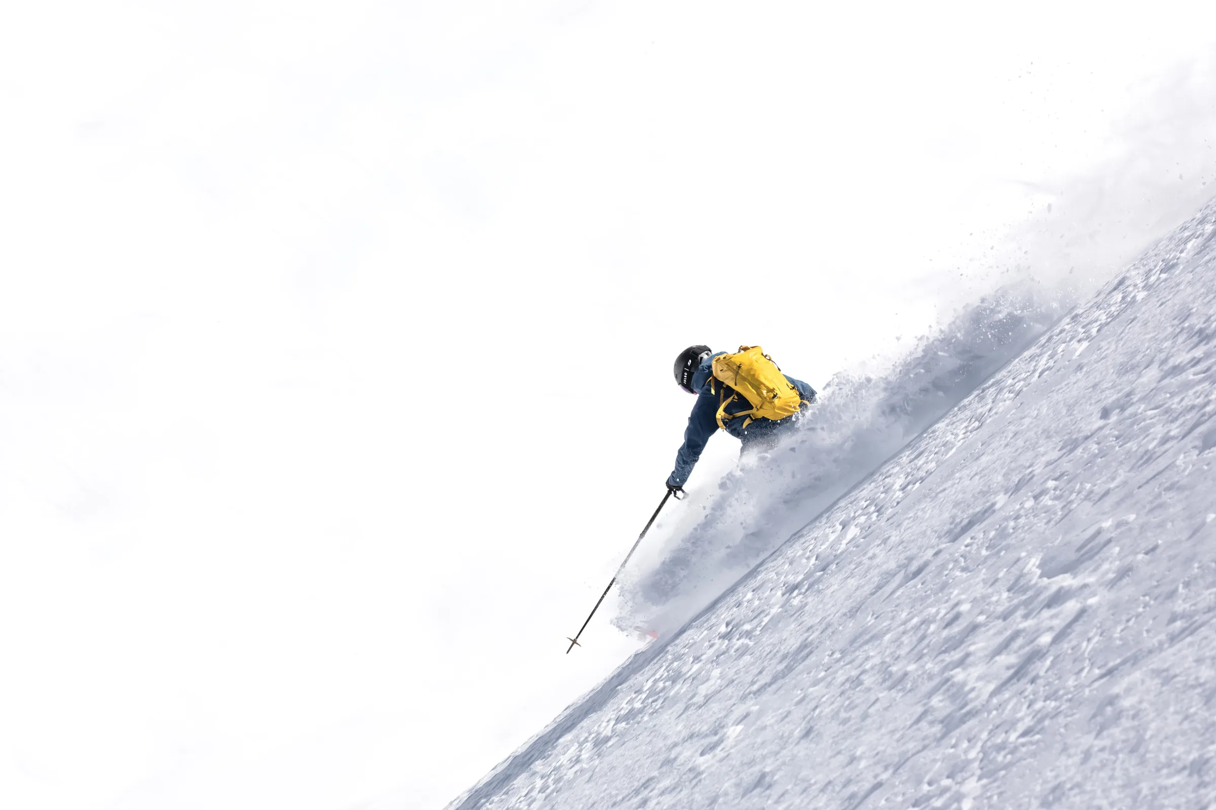 Von hinten gesehen fährt Valentin Rapp mit gelbem Rucksack einen steilen Schneehang hinab und streckt einen Skistock talwärts, während Schnee hinter ihm aufspritzt.